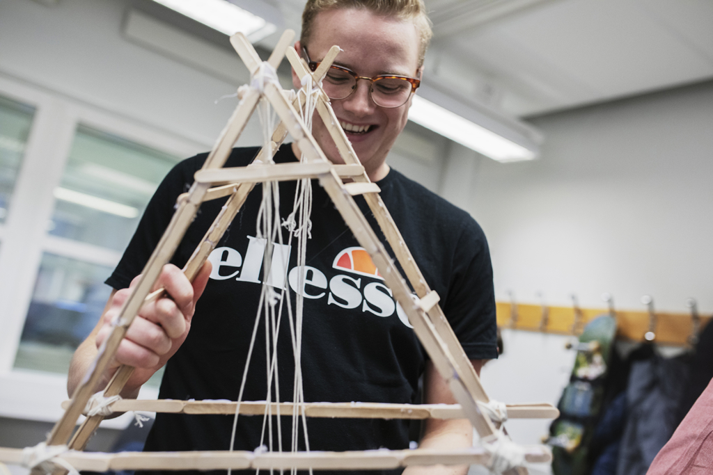 Manlig, glad studerande håller i en brokonstruktion gjord av glasspinnar.