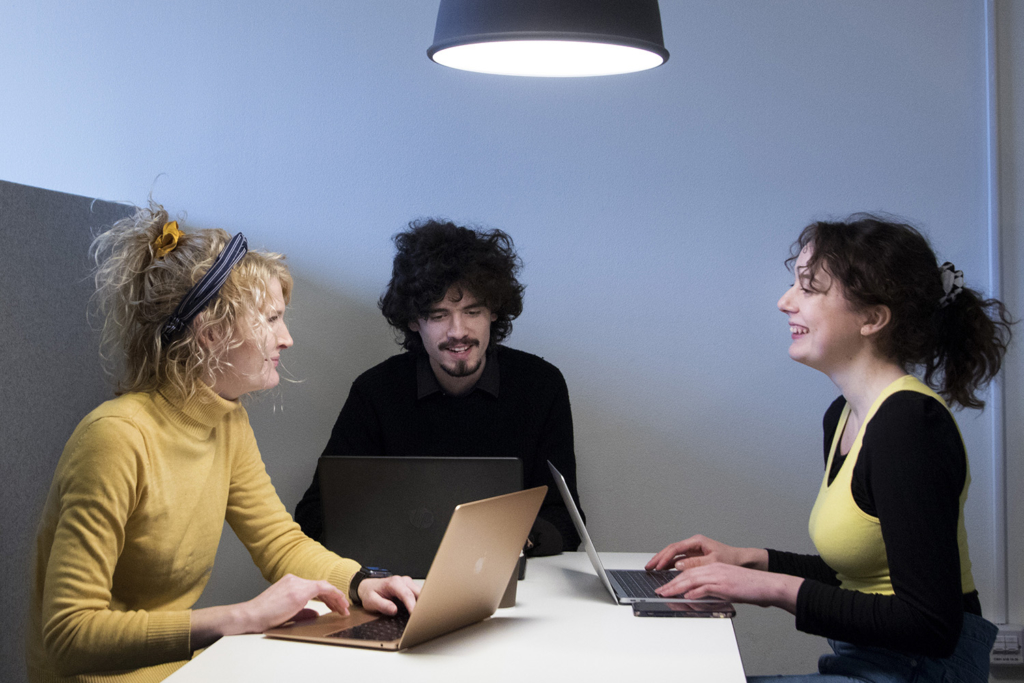 Tre glada studerande, en man och två kvinnor, sitter vid ett bord med varsin laptop.