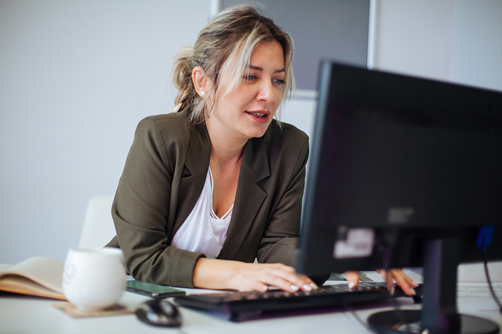Kvinna i kavaj sitter och arbetar framför en dator.