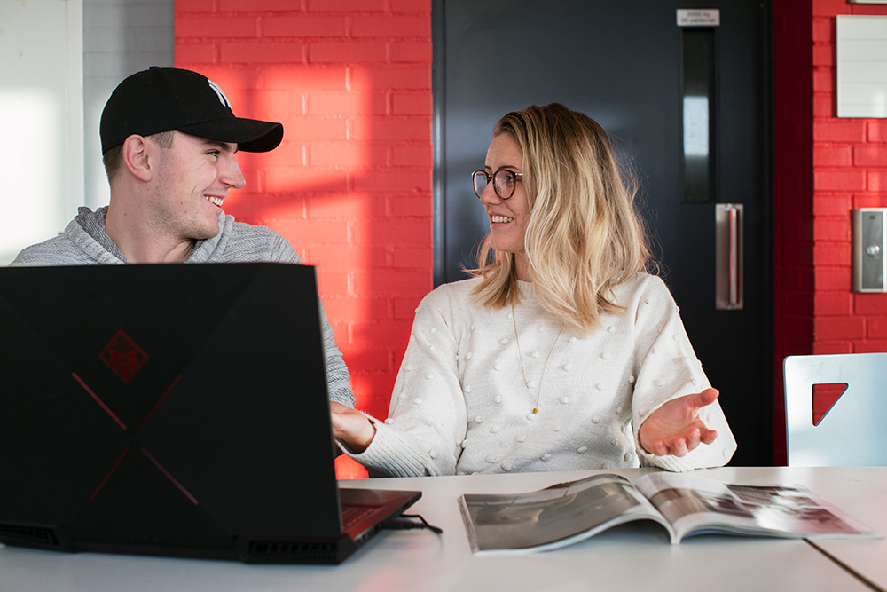 En kvinnlig och en manlig studerande sitter och diskuterar framför en dator.